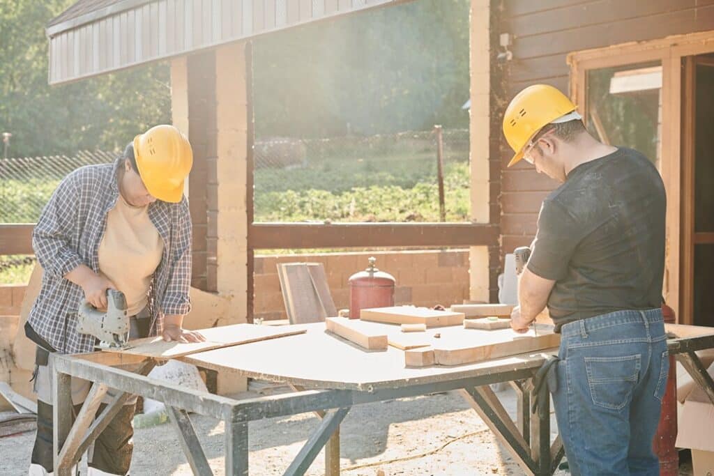 A handyman and woman drilling nail in wood outdoors
