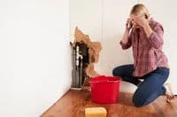 Two men are holding buckets and collecting water underneath from the leaking roof