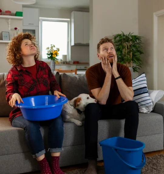 man and woman staring at roof leak with buckets by them